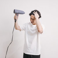 白シャツ姿でドライヤーで髪を乾かす男性のヘアセットの写真