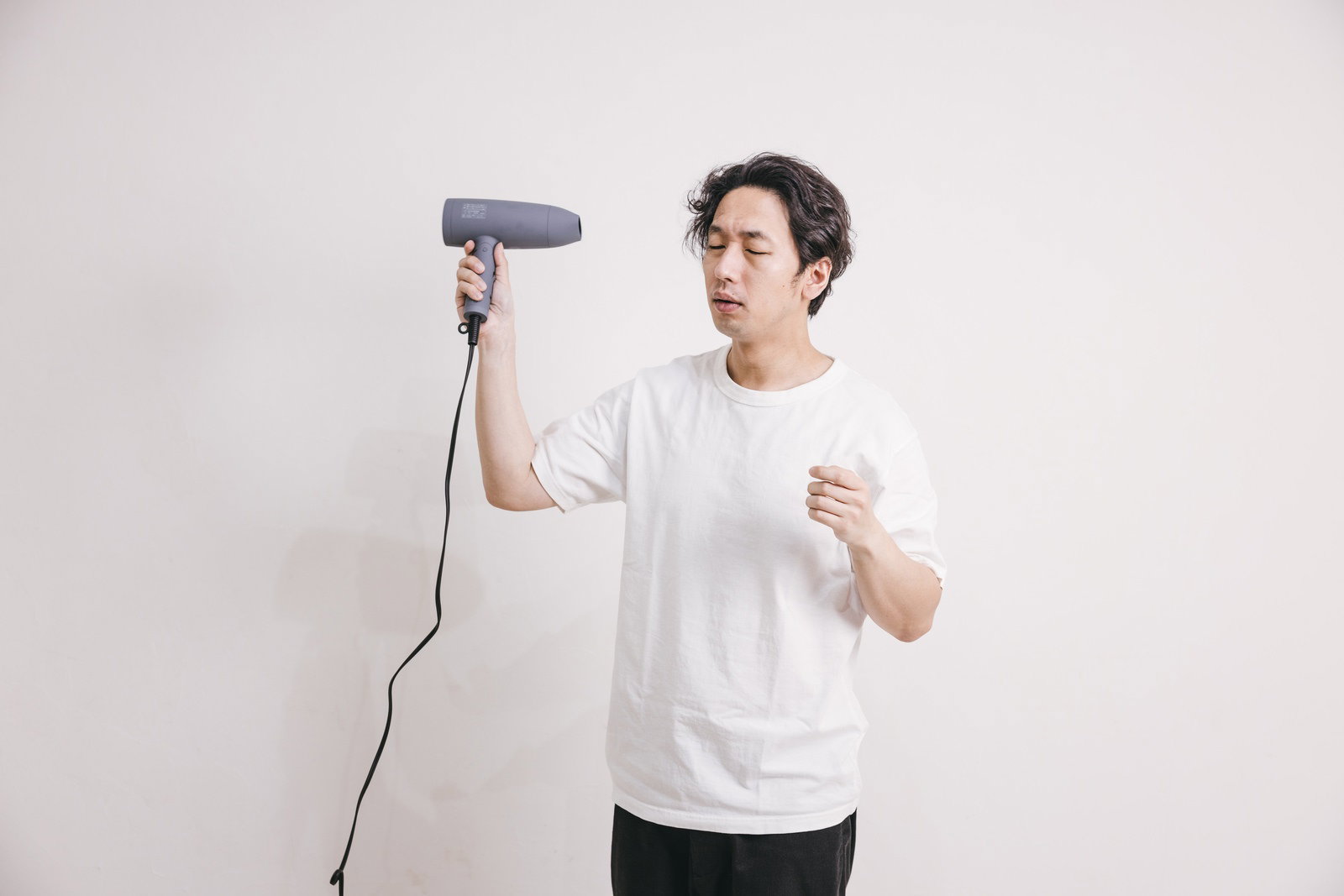 白いTシャツを着た男性がドライヤーで髪をブローしている［モデル：大川竜弥］