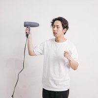 ドライヤーで髪をブローしている白Tシャツの男性の写真