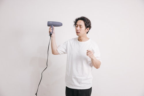 ドライヤーで髪をブローしている白Tシャツの男性
