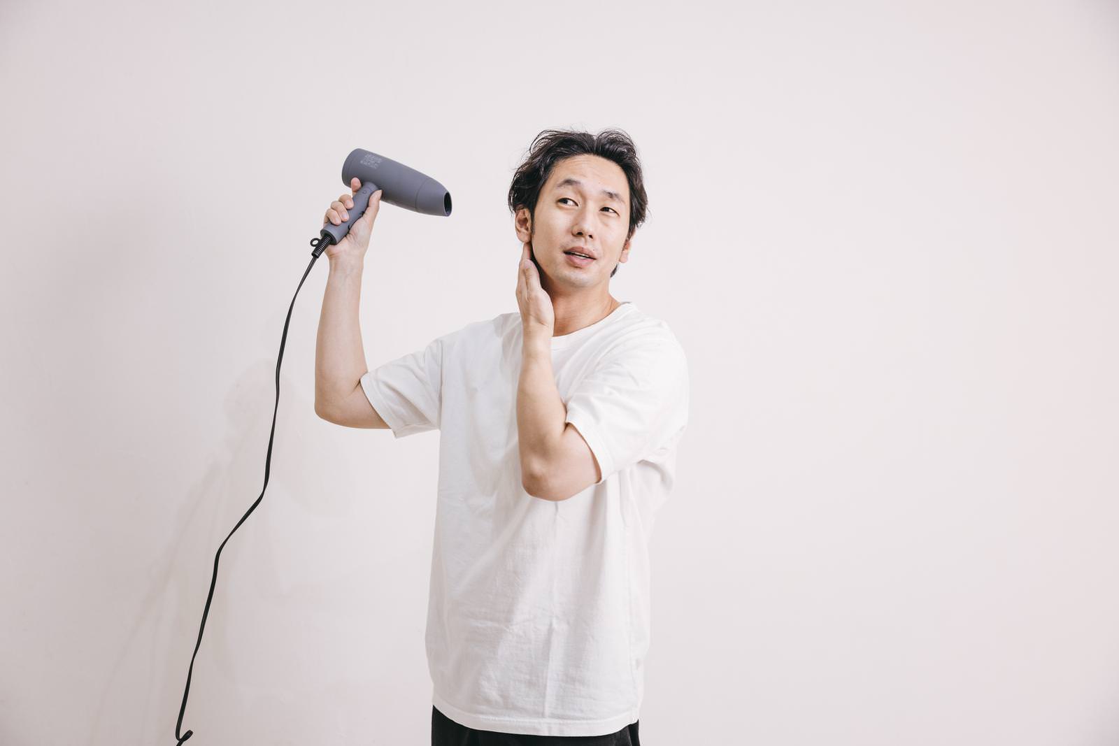 ドライヤーで髪をブローする白いTシャツの男性［モデル：大川竜弥］
