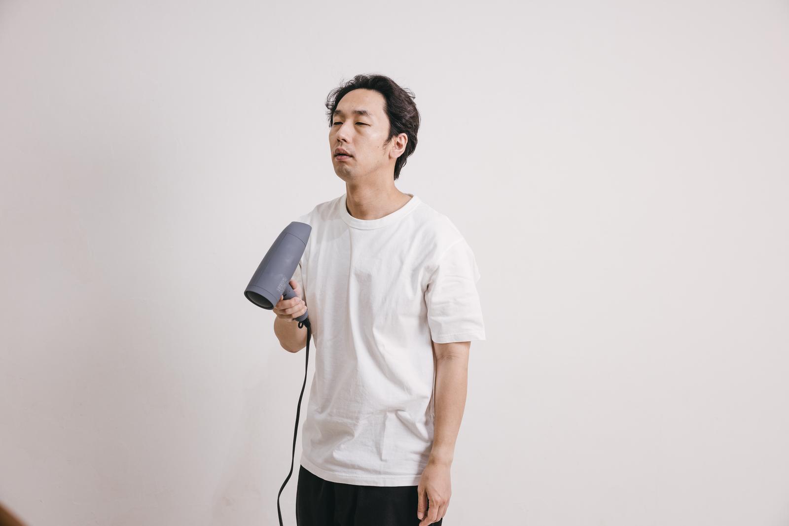 ドライヤーで髪をセットしている白いTシャツの男性［モデル：大川竜弥］