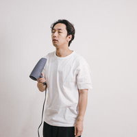 寝起きで頭がぼーっとしながらドライヤーでヘアセットする男性の写真