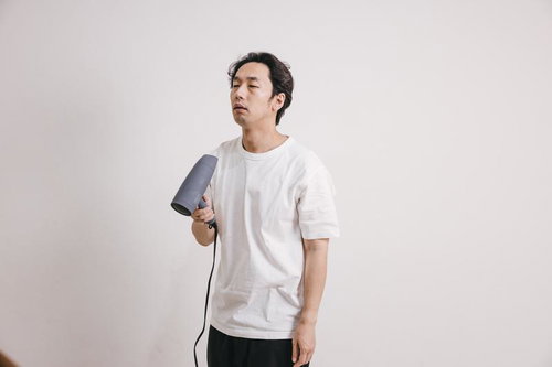 寝起きで頭がぼーっとしながらドライヤーでヘアセットする男性