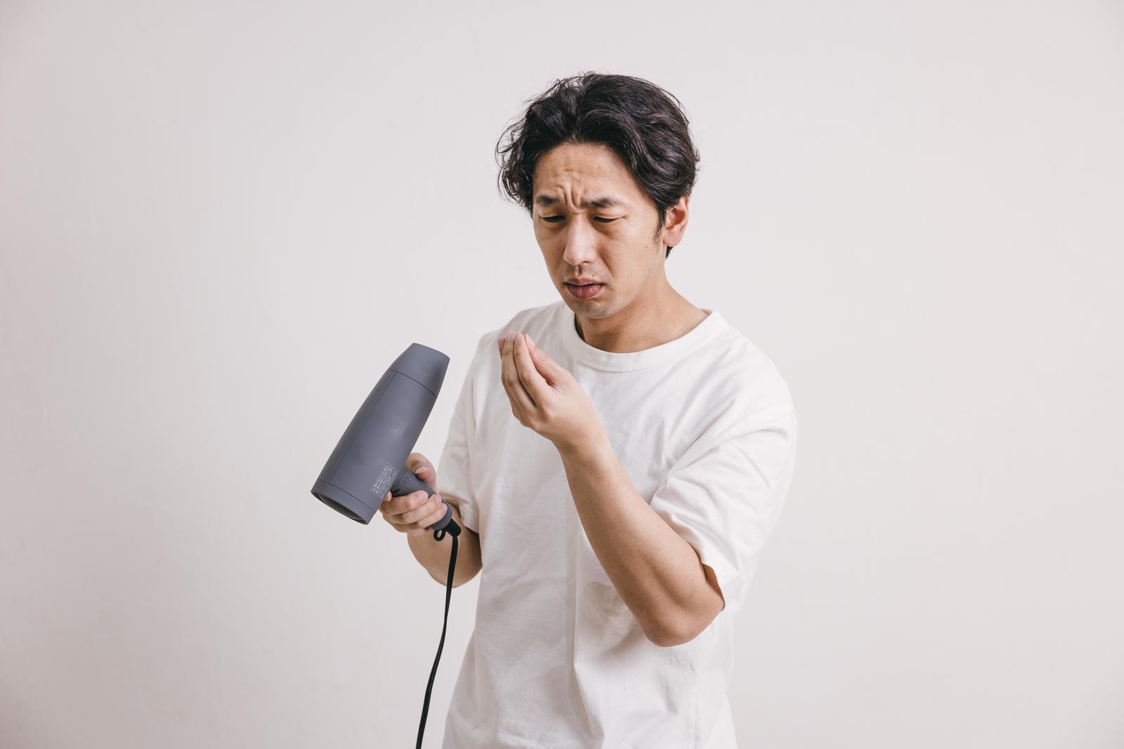 ドライヤーを持ちながら抜け毛を気にして心配そうな表情をする中年男性［モデル：大川竜弥］