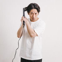 黒いヘアアイロンを使う不安そうな表情の男性の写真