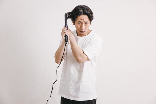 黒いヘアアイロンを使う不安そうな表情の男性