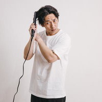 ヘアアイロンで髪をセットする白Tシャツと黒ズボンの男性の写真