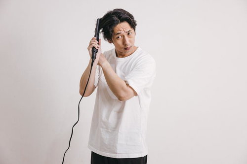 ヘアアイロンで髪をセットする白Tシャツと黒ズボンの男性