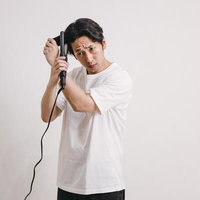 ヘアアイロンに寝癖部分を挟み込む男性の写真