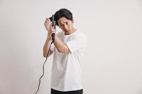 ヘアアイロンに寝癖部分を挟み込む男性