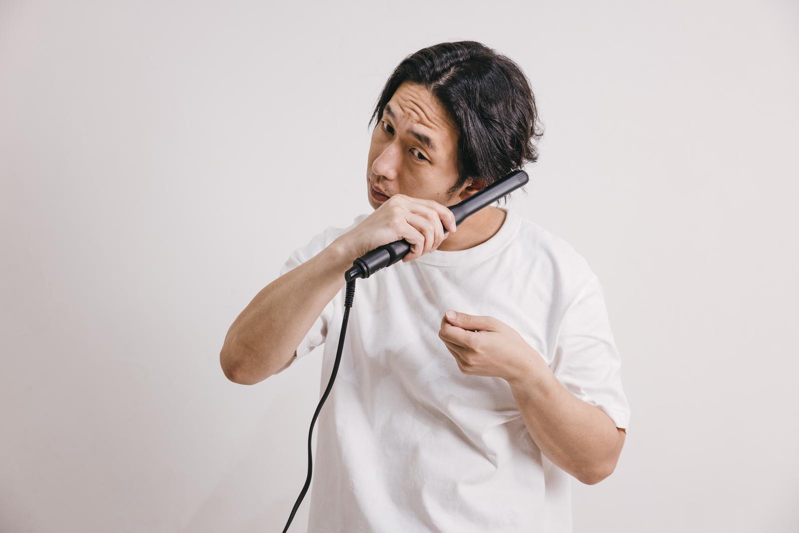 白Tシャツの男性がヘアアイロンで髪の毛をストレートにセットしている［モデル：大川竜弥］