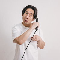 ヘアアイロンを髪に当てる白Tシャツの男性の写真