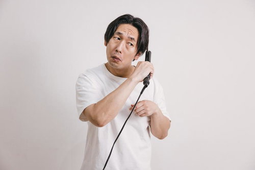 ヘアアイロンを髪に当てる白Tシャツの男性