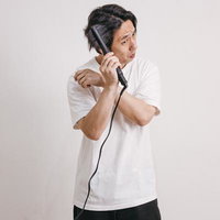 ヘアアイロンで髪をセットする白Tシャツの男性の写真