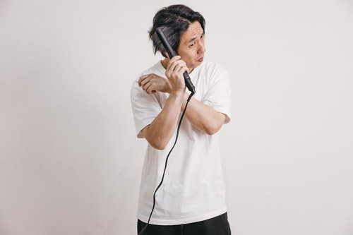 ヘアアイロンで髪をセットする白Tシャツの男性