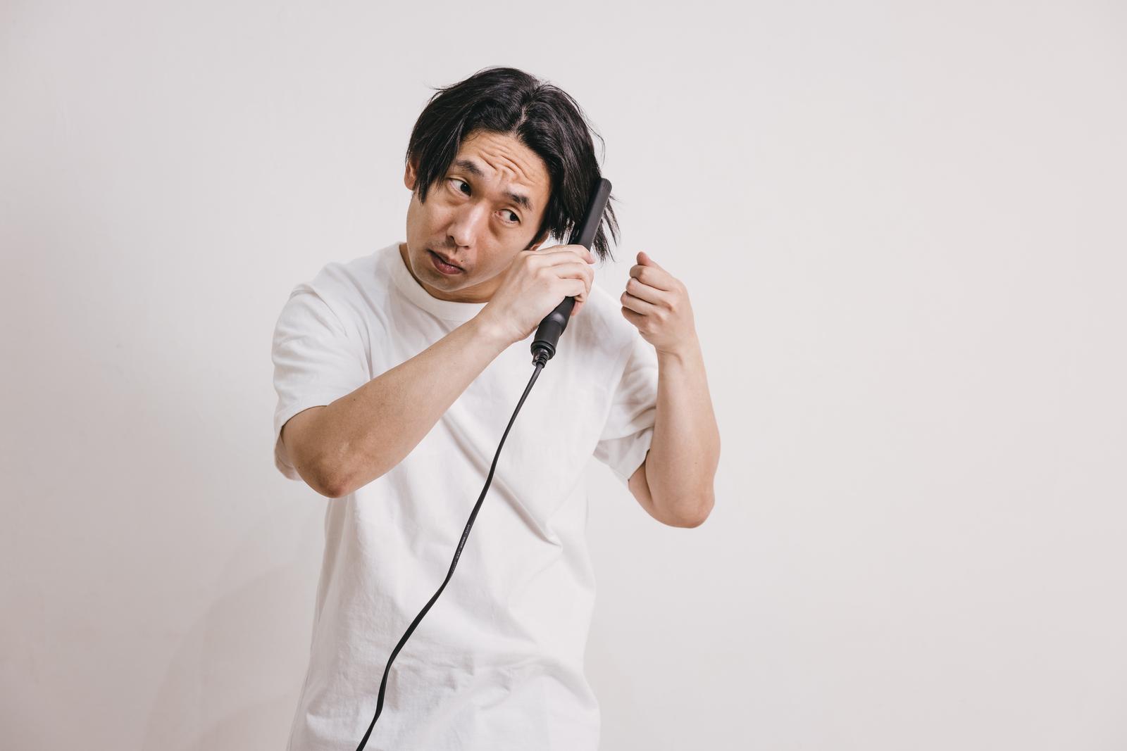 ヘアアイロンで寝癖を直している白いシャツの男性［モデル：大川竜弥］