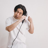 ヘアアイロンで寝癖を直す白いシャツの男性の写真