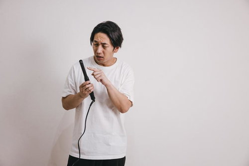 ヘアアイロンの高温部分に指を近づける男性