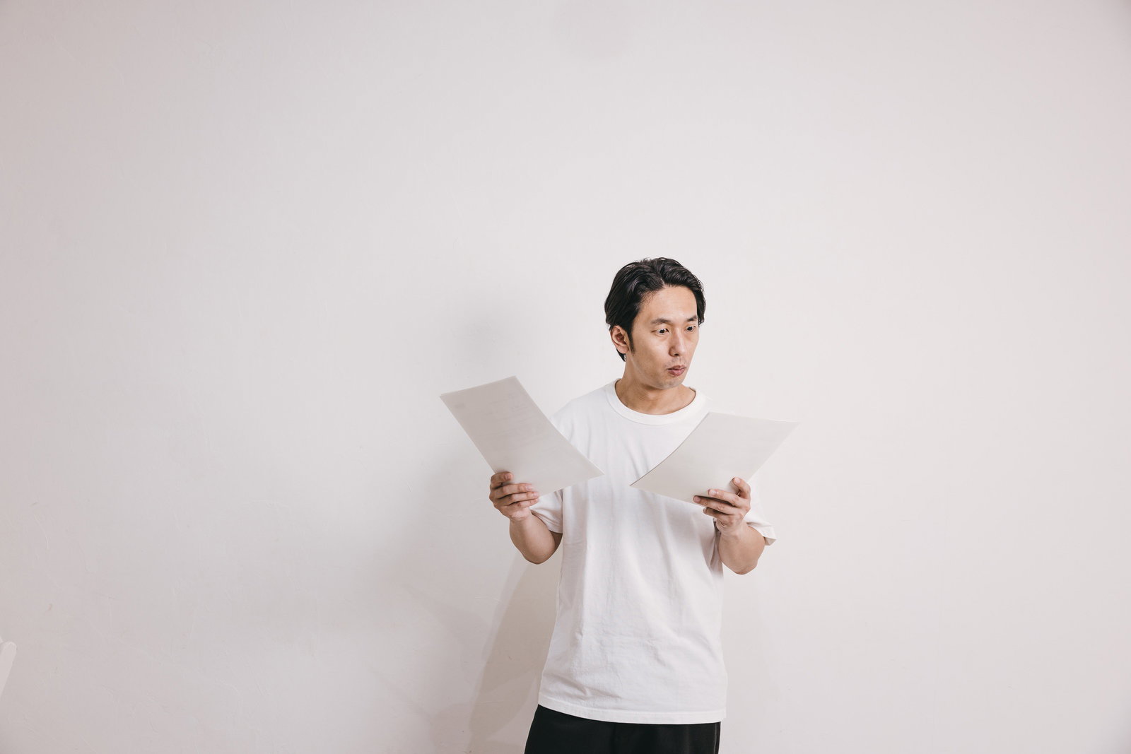 健康診断の結果を見て驚いた表情を浮かべる白い服の男性［モデル：大川竜弥］