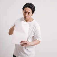 白い封筒を恐る恐る開ける男性の不安な表情の写真