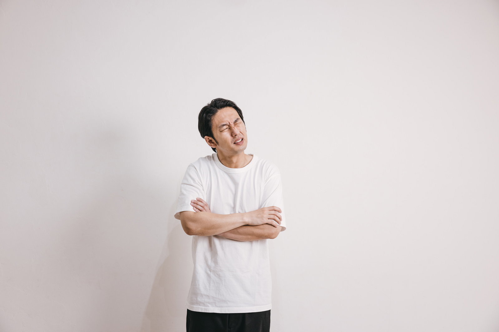 白いTシャツを着て腕を組み、悪寒を感じている男性［モデル：大川竜弥］