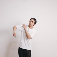 肩の痛みを感じる四十肩の男性、白いTシャツで肩こりと疲労を表現の写真