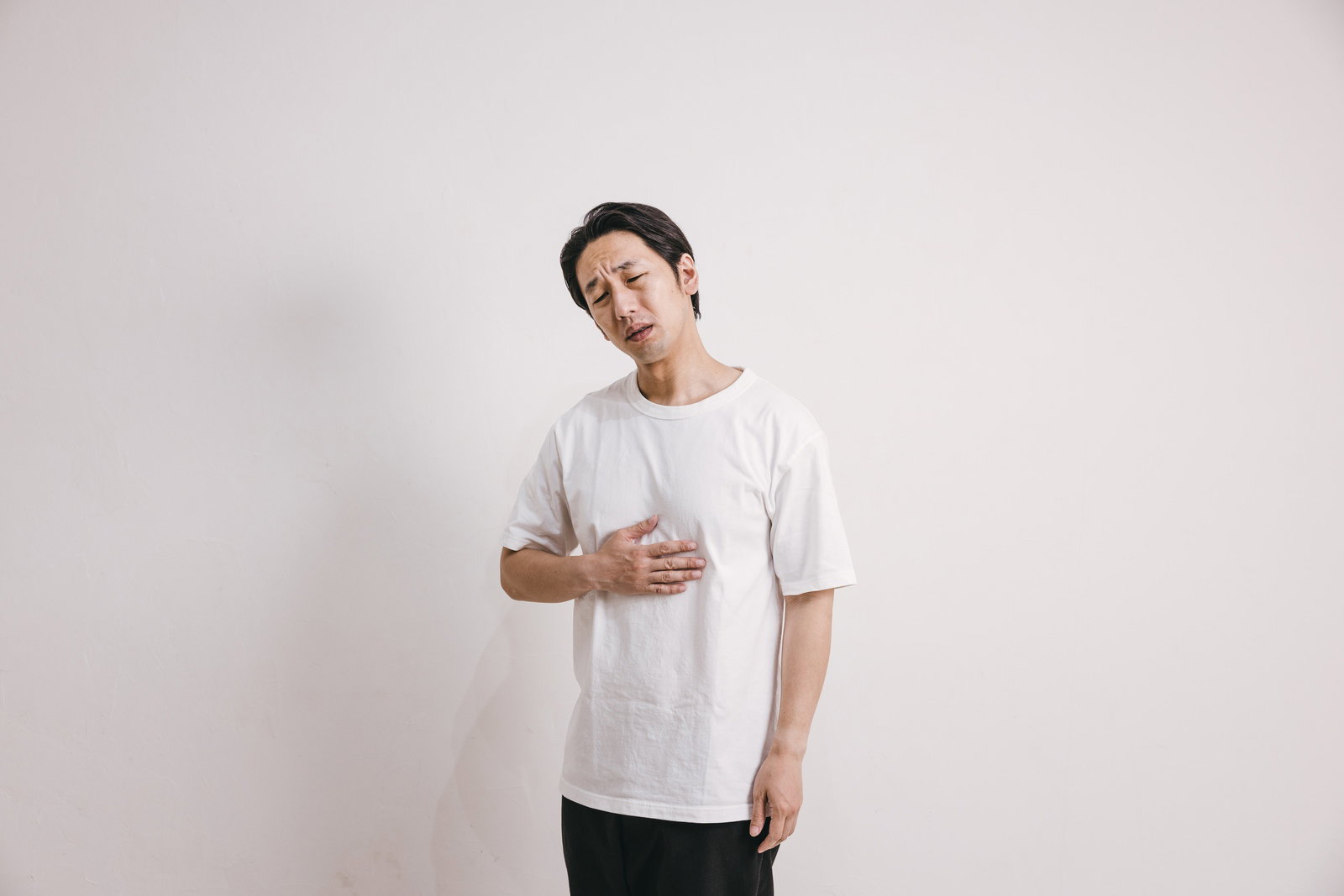 みぞおちに手を当てて苦しむ男性［モデル：大川竜弥］