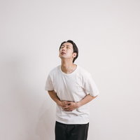 白いTシャツの男性が腹部を押さえて苦しむ胃腸炎の写真