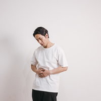 ストレスで胃が痛い男性、白いTシャツで腹痛を表現の写真