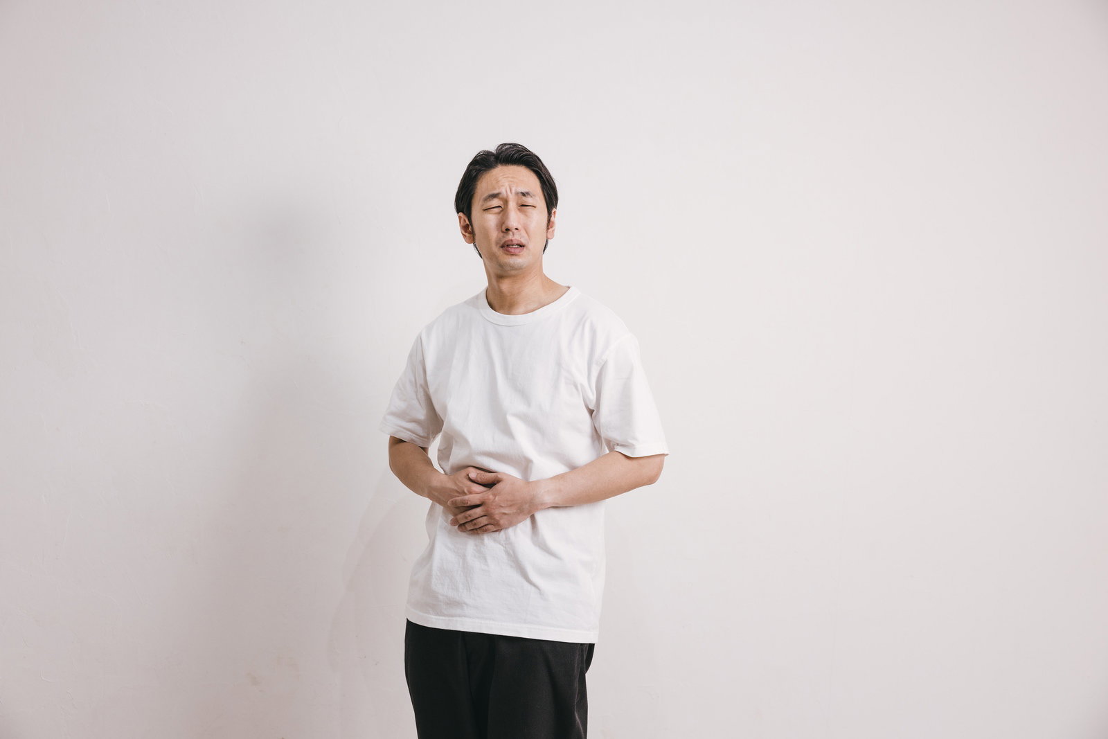 白いTシャツを着た男性が腹部を押さえて苦痛の表情をしている［モデル：大川竜弥］