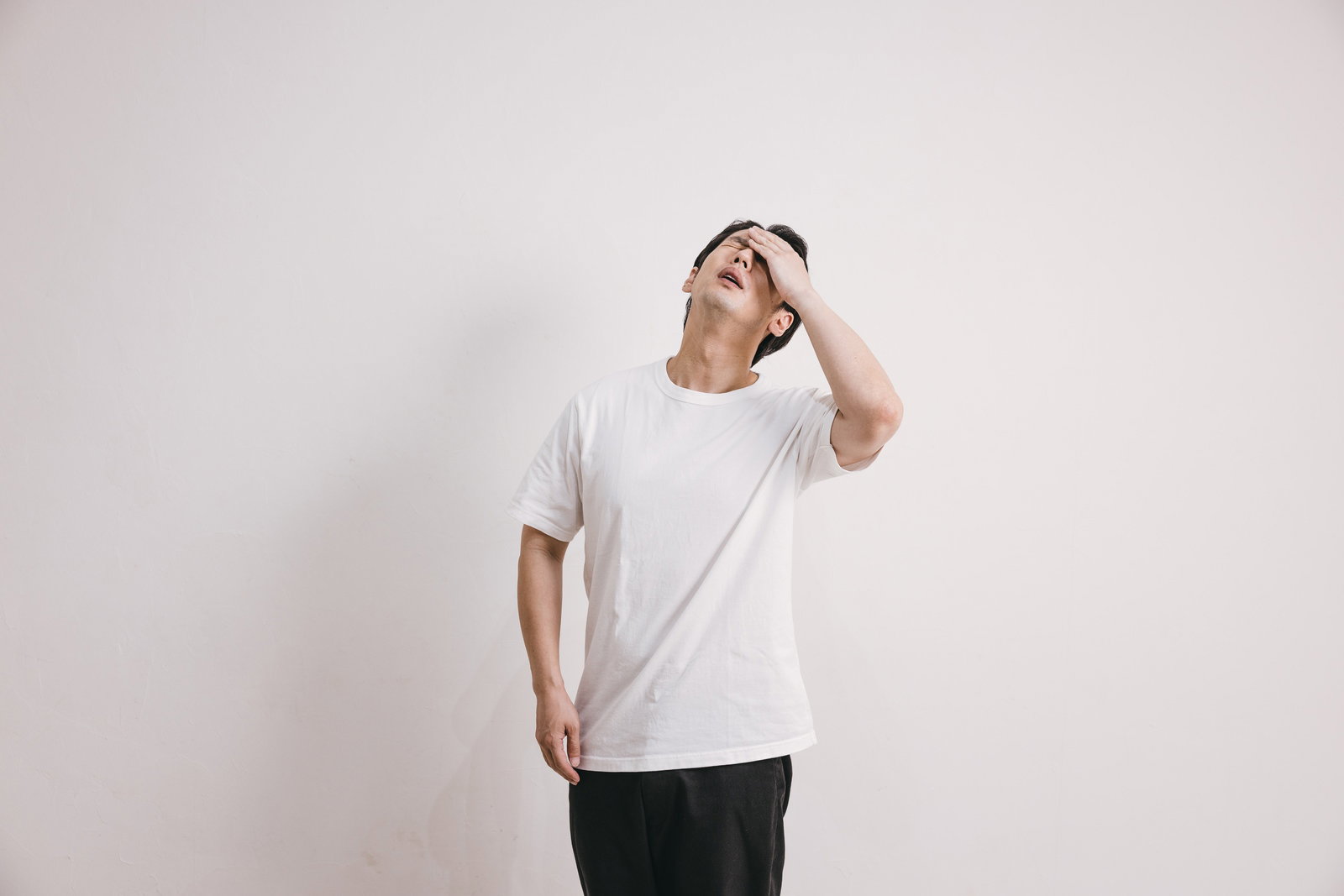 額に手を当てて上を向く男性［モデル：大川竜弥］