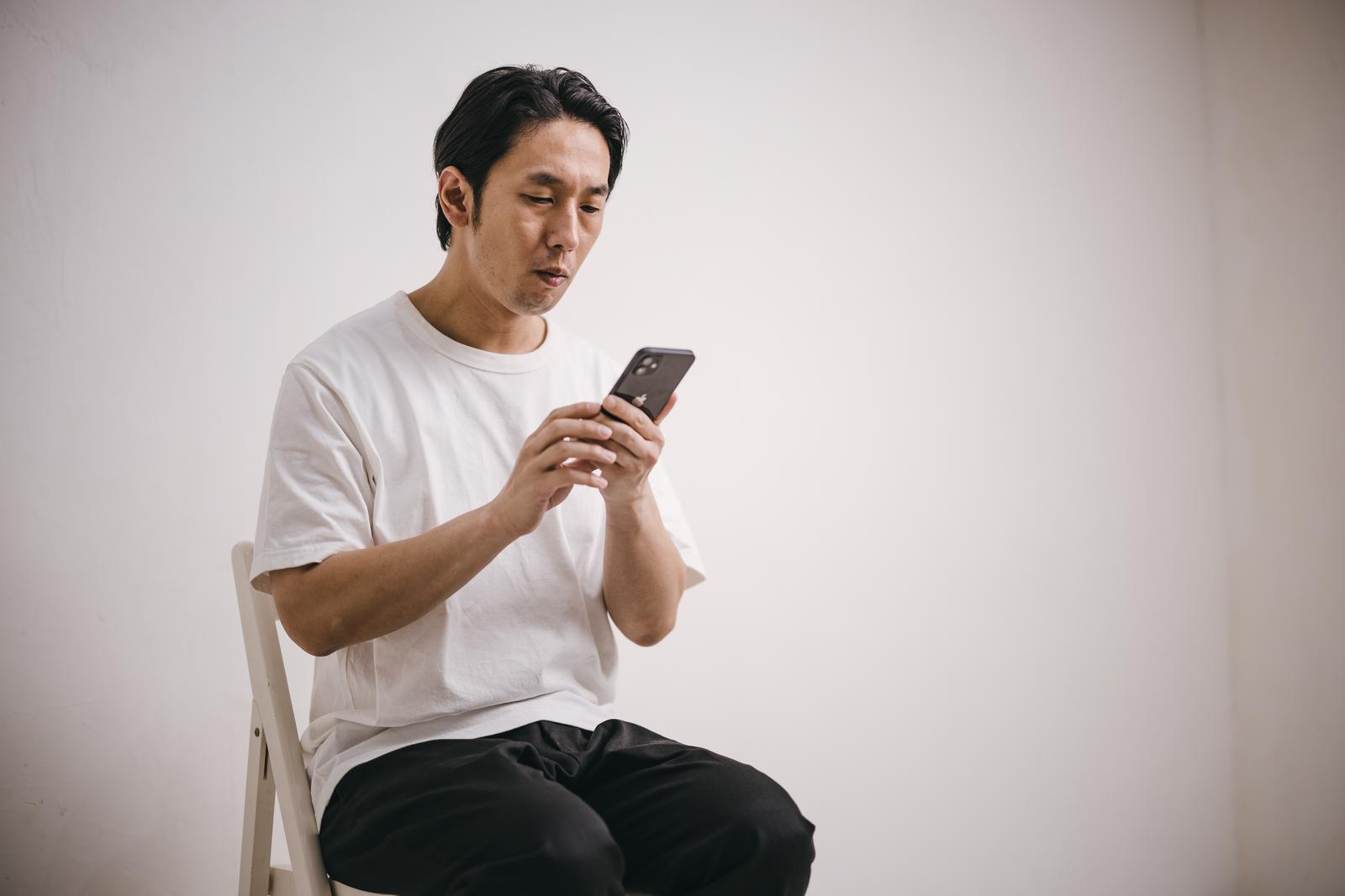 白いTシャツを着てスマートフォンを見つめる男性［モデル：大川竜弥］