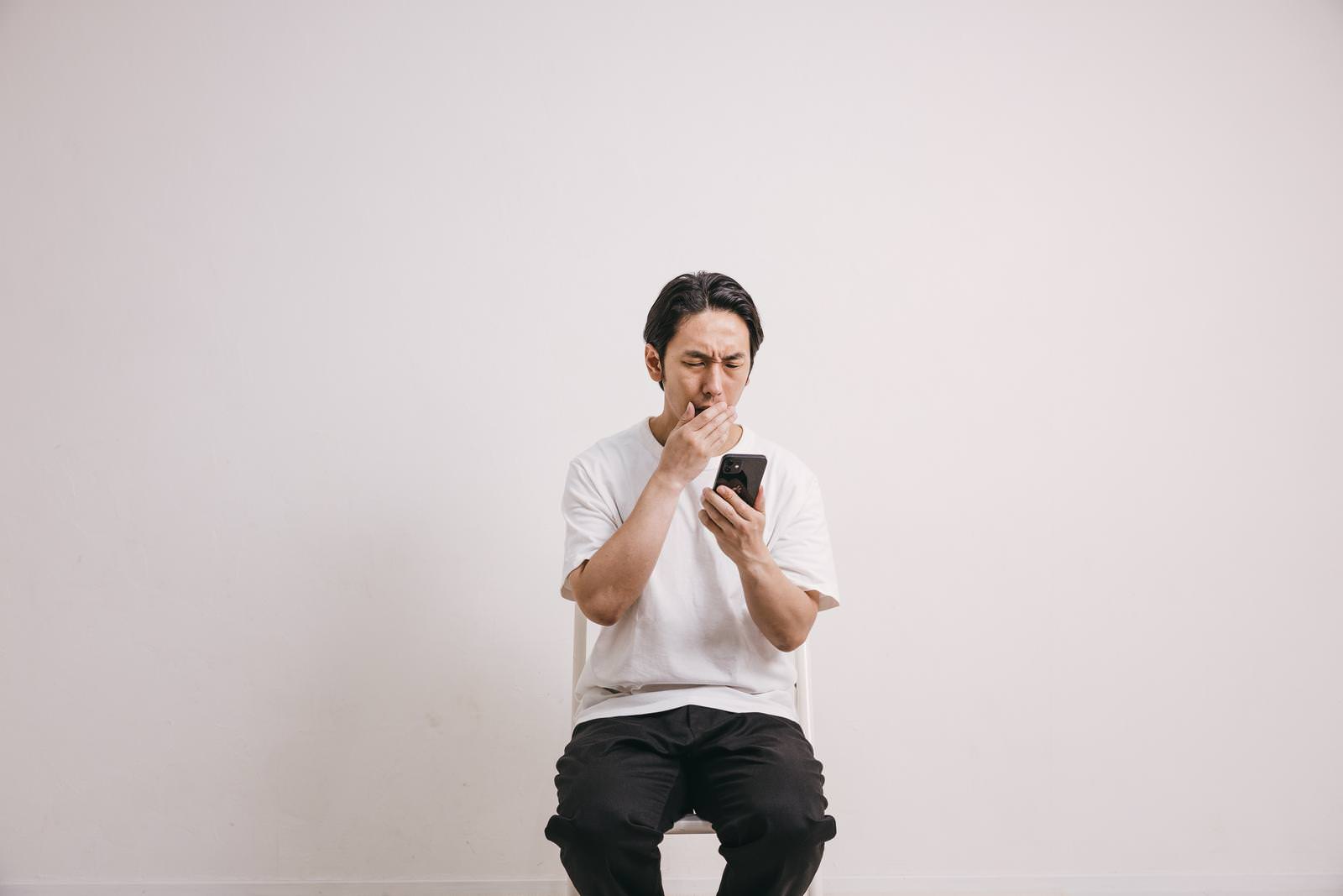 白いTシャツを着た男性がスマートフォンを見て驚いている様子［モデル：大川竜弥］