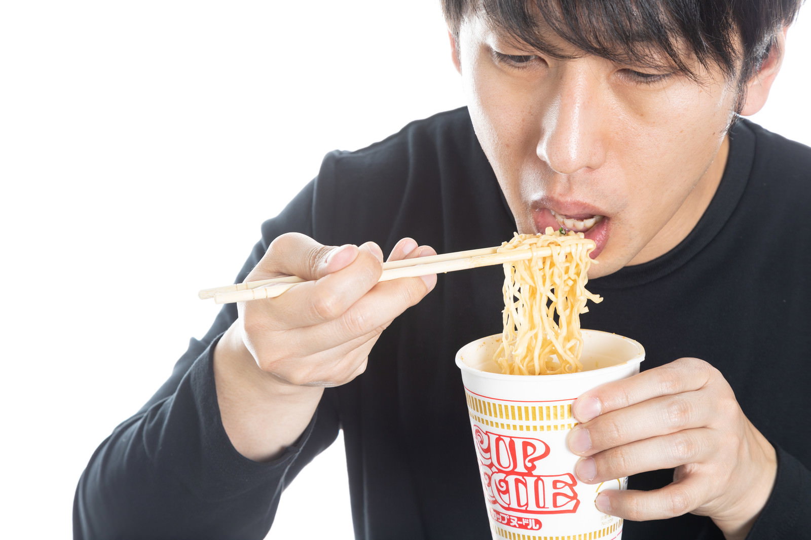 黒いスーツを着た男性がカップラーメンを箸で食べている［モデル：大川竜弥］