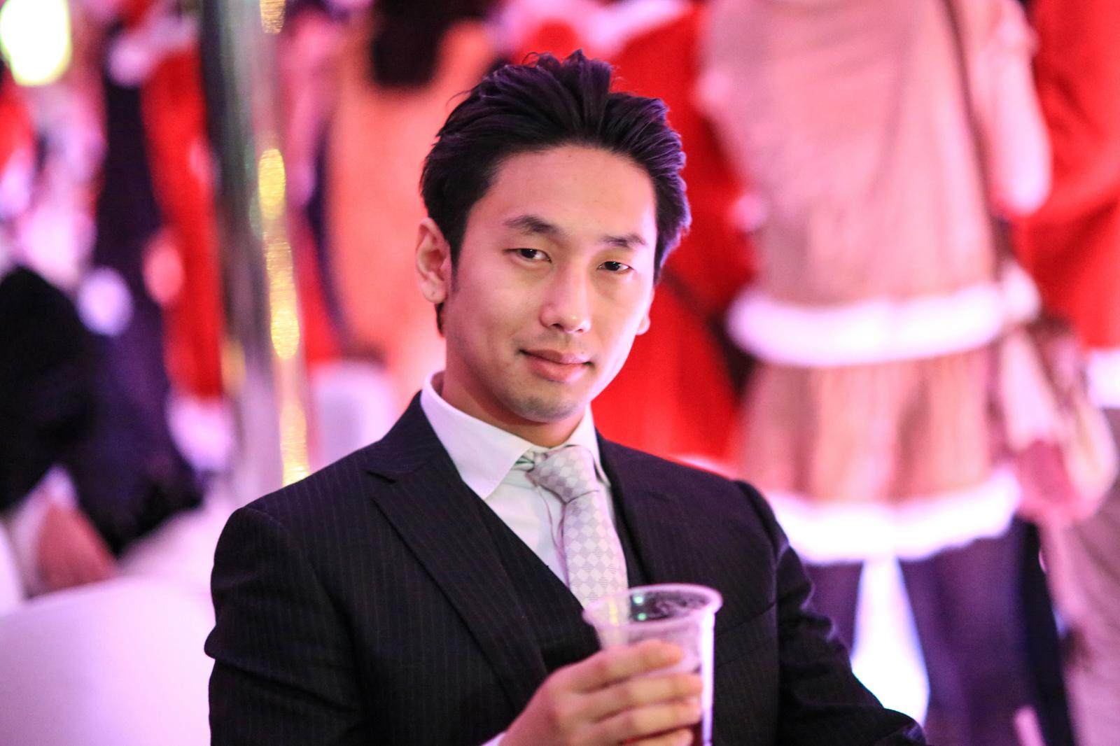パーティー会場でカクテルを持つスーツ姿の男性［モデル：大川竜弥］
