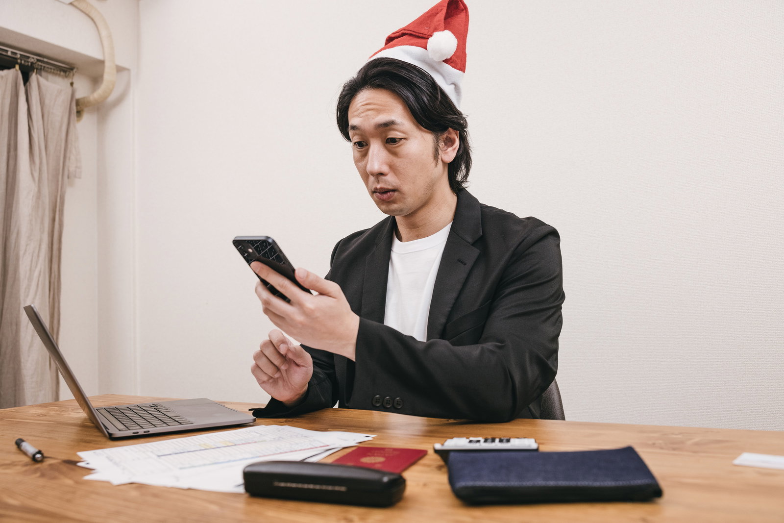 サンタ帽をかぶってスマホを見る残業中の男性［モデル：大川竜弥］