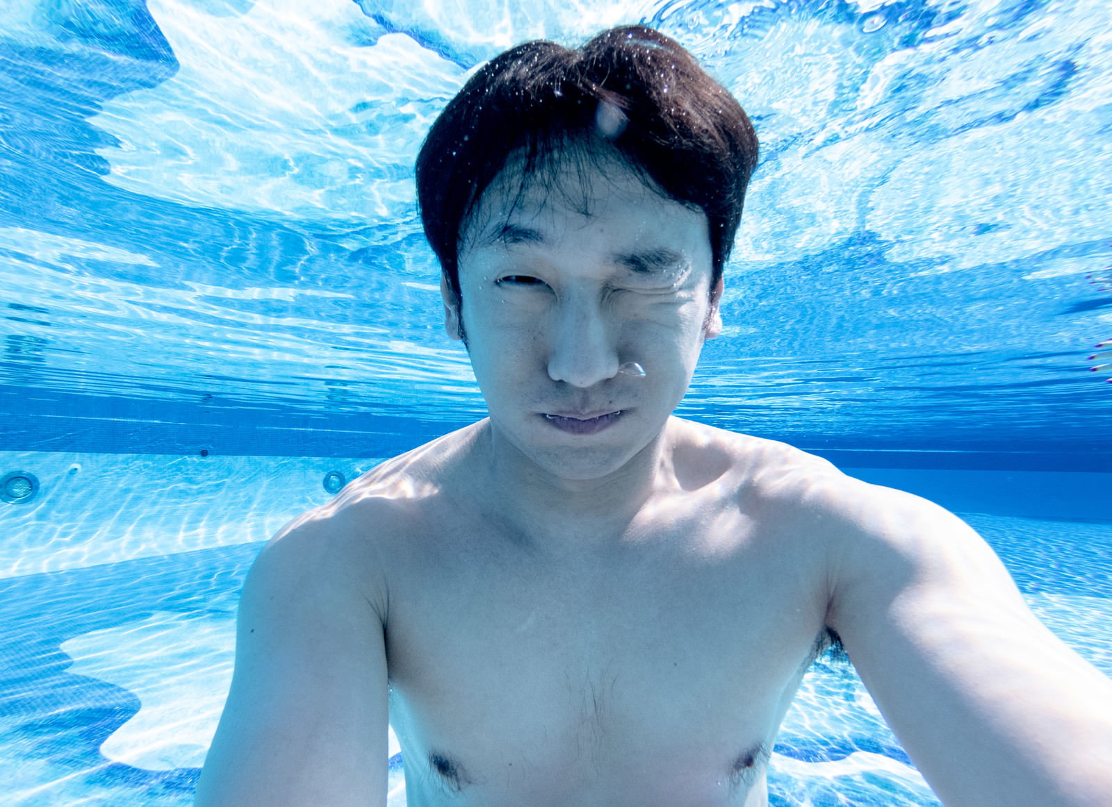 プールの水中で自撮りをする男性と立ち上る気泡［モデル：大川竜弥］