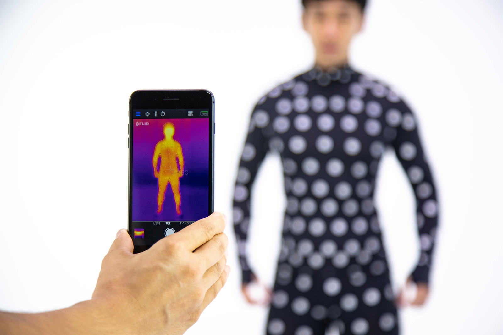 スマホでサーモグラフィーカメラを使い採寸ボディースーツを撮影する手元［モデル：大川竜弥］