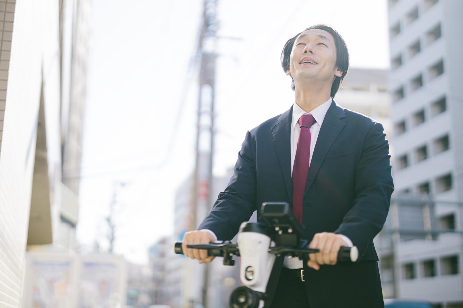都市部でスーツ姿の男性が電動キックボードで走行している［モデル：大川竜弥］