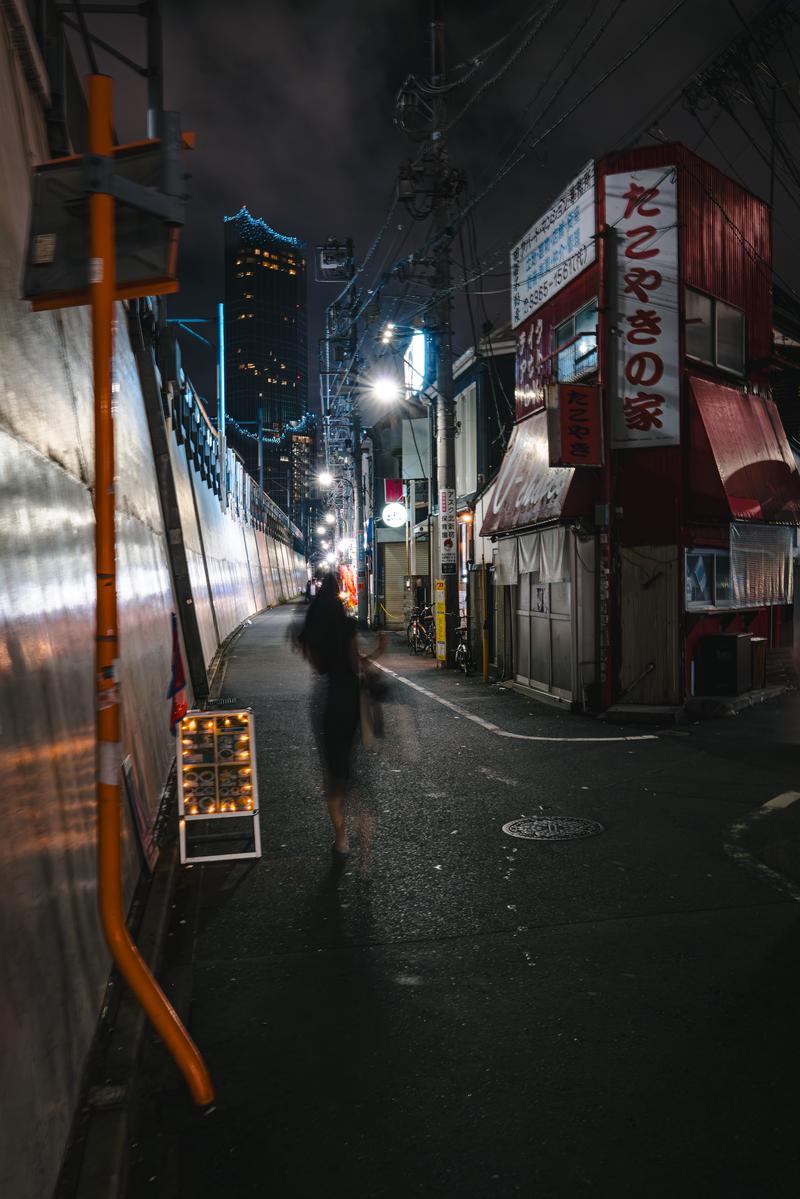 夜の新宿区百人町の路地裏を歩く人物と飲食店の看板