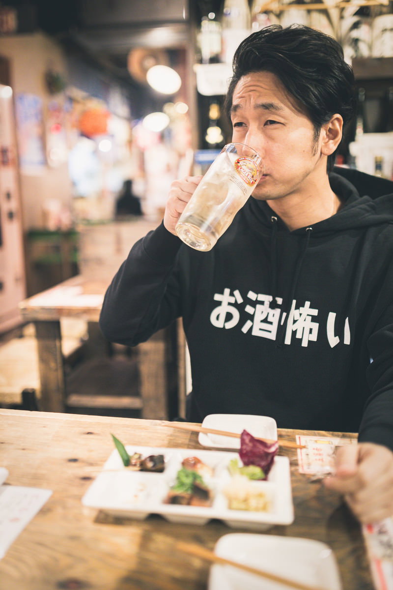 居酒屋でハイボールを飲む黒いTシャツの男性［モデル：大川竜弥］