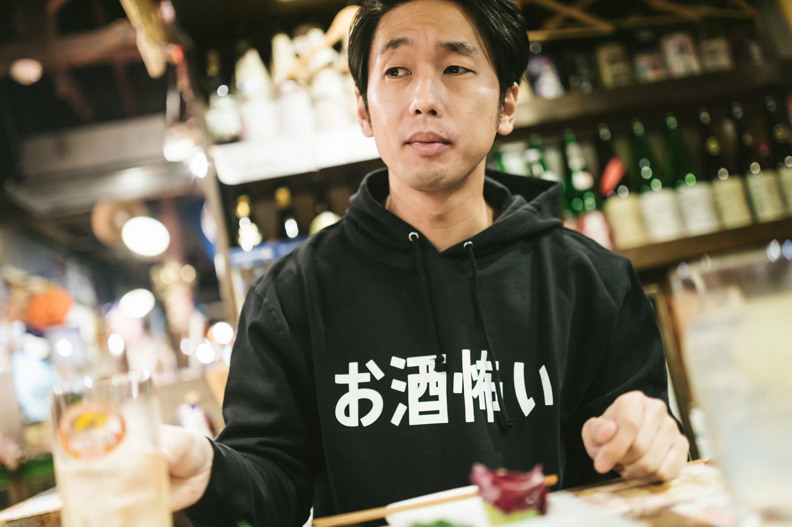 お酒怖いと書かれた黒いパーカーを着てハイボールを飲む男性［モデル：大川竜弥］
