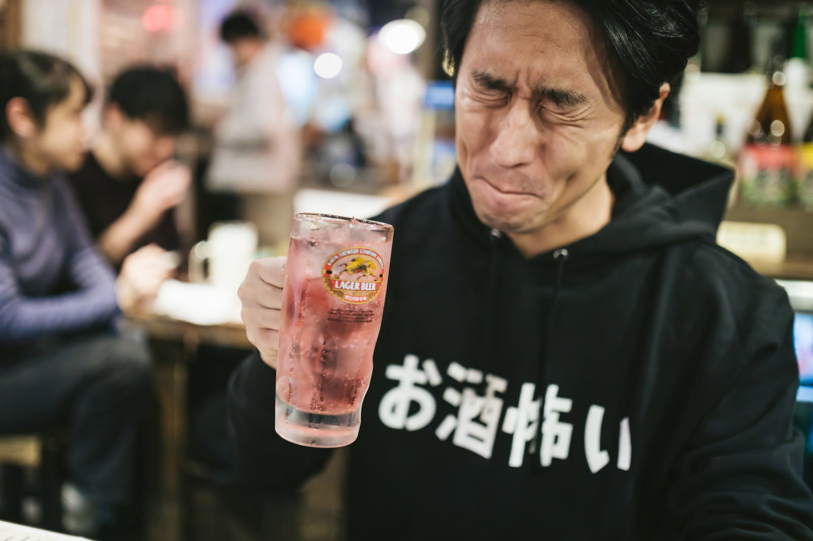 ピンク色のチューハイを手に持つ黒いフードパーカーの男性［モデル：大川竜弥］