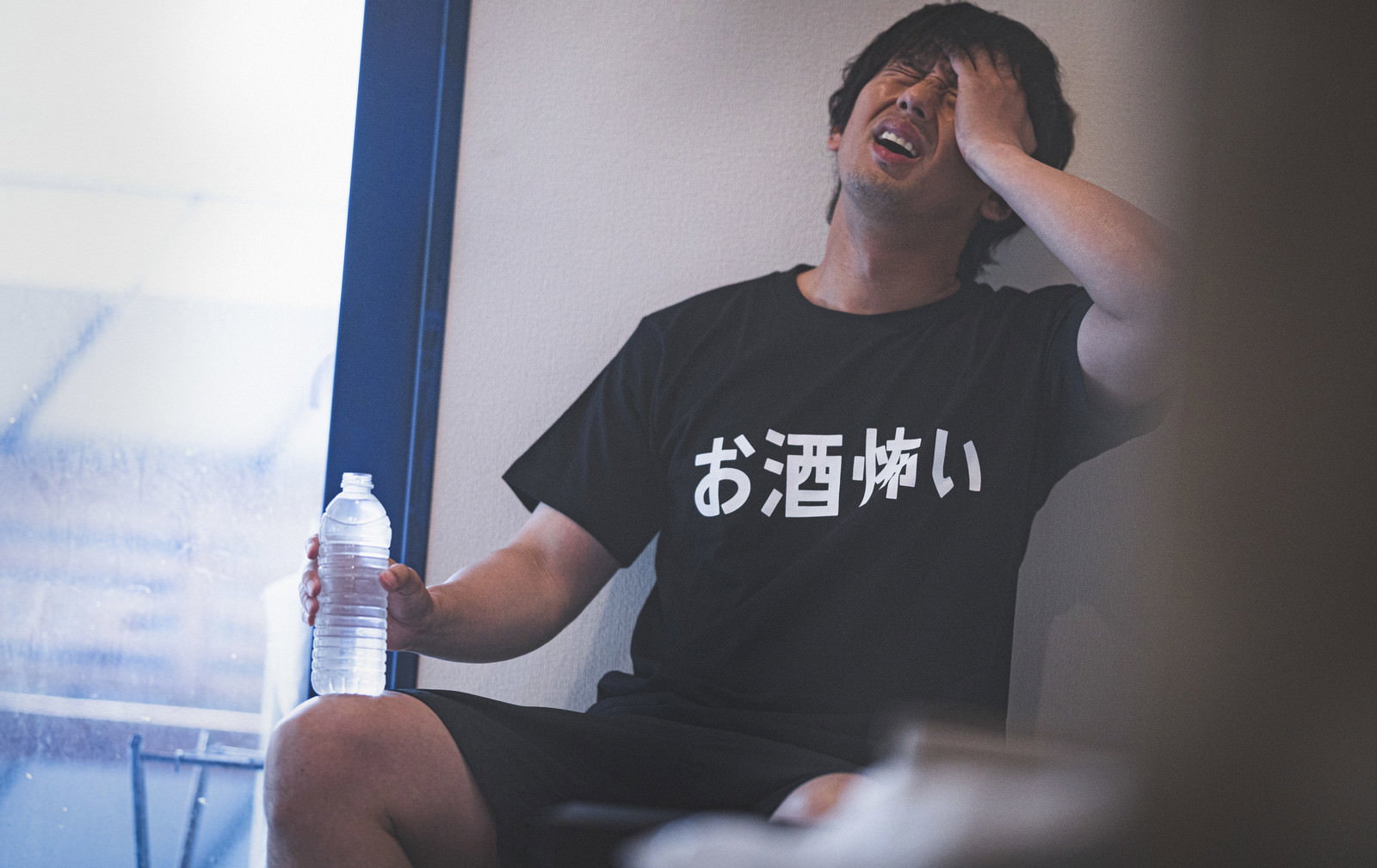 黒いTシャツを着た男性が二日酔いで頭を抱えている［モデル：大川竜弥］