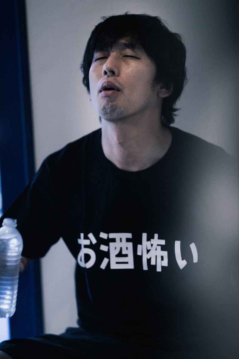 黒いTシャツの男性が目を閉じて口元に手を当て、二日酔いの吐き気に苦しむ表情［モデル：大川竜弥］