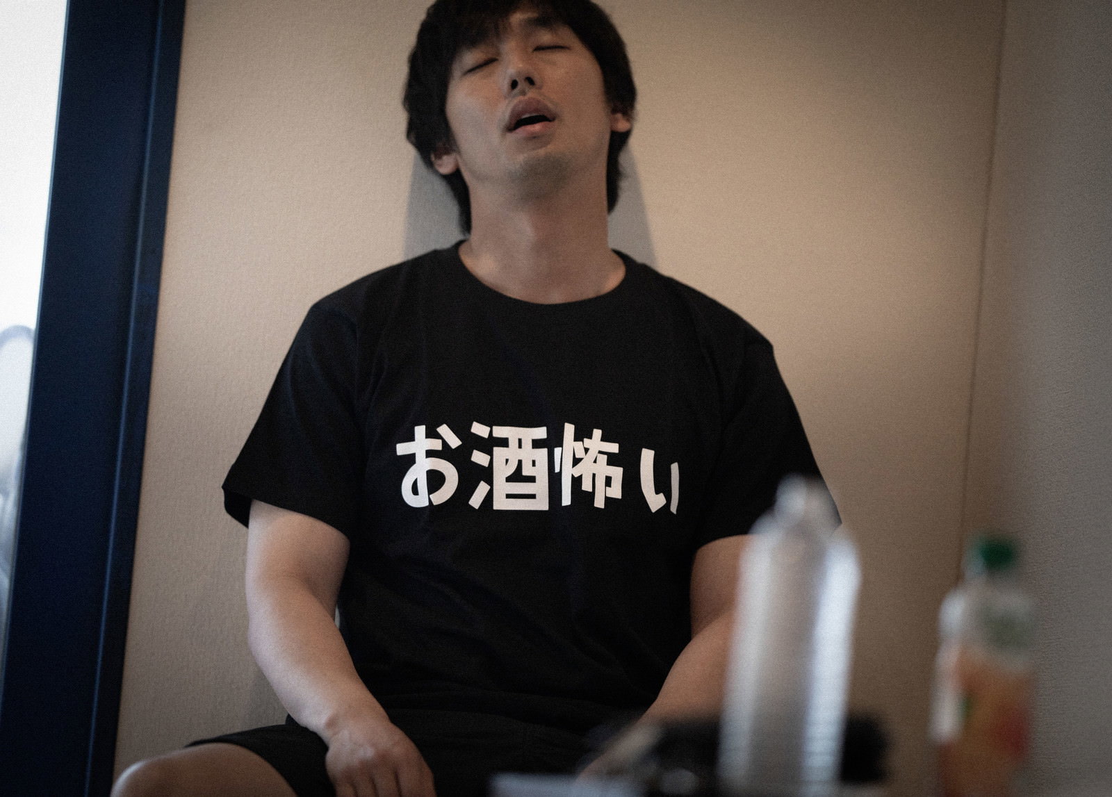 お酒怖いと書かれた黒いTシャツを着て椅子に座る男性［モデル：大川竜弥］