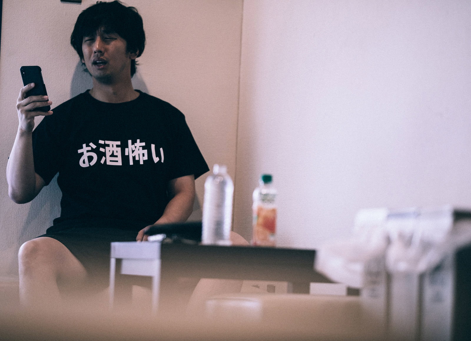 二日酔いの状態でスマートフォンを手に持つ黒いTシャツの男性［モデル：大川竜弥］