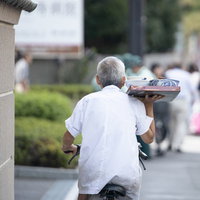 片手で出前を運ぶ職人の自転車配達員が走行する配達シーンの写真