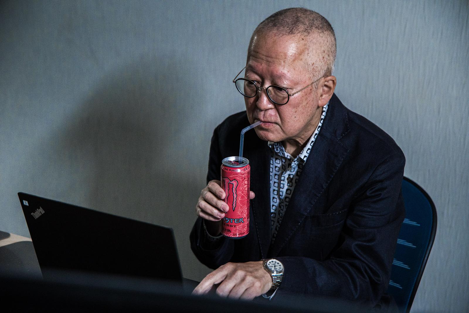 ストローでピンモンを飲みながらノートパソコンを操作する眼鏡の高齢男性［モデル：渡辺カンジ］